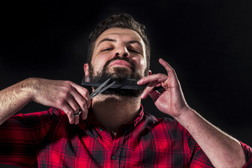 Young man trimming his beard with comb and scissors