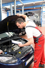 Fototapeta na wymiar KFZ Mechaniker kontrolliert Auto in einer Werkstatt // Automotive mechanic controlled car in a workshop