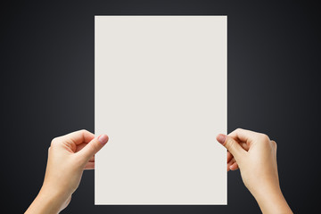 Hands holding a white paper blank isolated on black background.