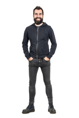 Laughing bearded punker in black hoodie with hands in pockets looking at camera. Full body length...