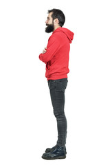 Side view of bearded young man in red hoodie with crossed arms looking away. Full body length portrait isolated over white studio background. 