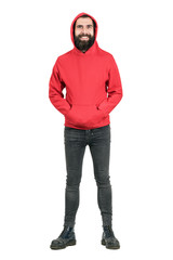 Laughing bearded punker wearing red hoodie looking at camera with hands in pockets. Full body...