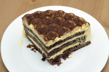 For breakfast. A piece of sponge cake on a white plate on the wooden table surface. Closeup view