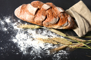 rustic crusty bread and wheat ears on a dark wooden table