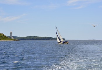 Naklejka premium small sailboat sailing along Georges Island near the light house, Halifax, Nova Scotia Canada