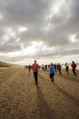 unrecognizable people in colorful outfits are running on a beach during the half marathon of Egmond. 