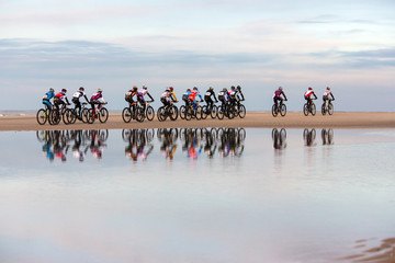 unrecognizable people drive with mountain bikes on a beach during a contest. with a visible...