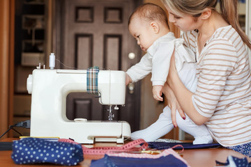Small child learns new knowledge, along with his mother inspects sewing machine. Work at home, parenting, parents and children, care, babysitter.