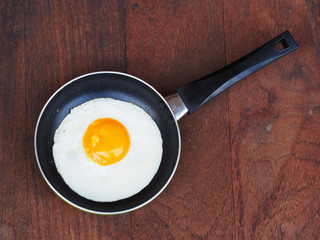 Fried eggs in a frying pan on wooden background
