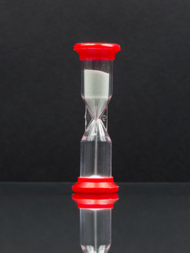 Small Red Hourglass With White Sand On Black Background With Reflexion
