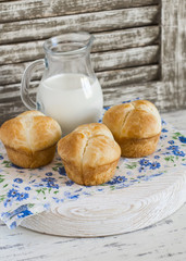 Homemade sweet brioche rolls and a pitcher of milk on a light rustic wood background