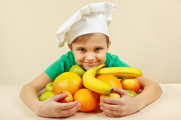 Little kid in chefs hat with fruits at the table