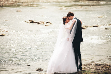 Fototapeta na wymiar Elegant gentle stylish groom and bride near river with stones. Wedding couple in love