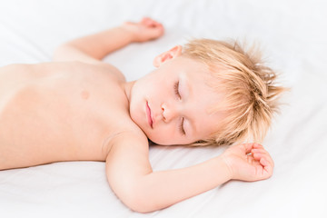 Obraz na płótnie Canvas Close-up portrait of little boy with blond hair sleeping on white bed. Carefree childhood concept