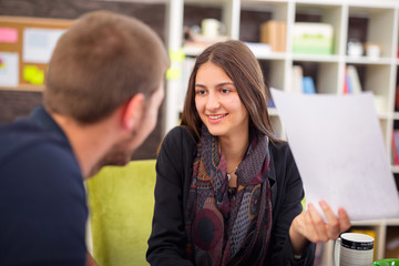 Fototapeta premium Beautiful smiling young businesswoman sitting working with a young man in a busy office