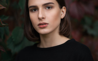 Closeup portrait of young elegant brunette hipster woman in black blouse against slight blurred ivy...