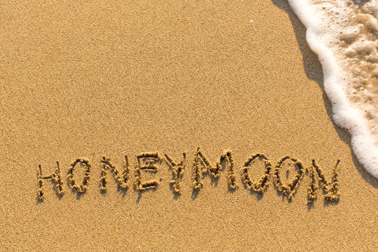Inscription Honeymoon on the sea beach sand, with the wave.