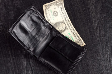 Black leather wallet with one dollar. Concept: poverty