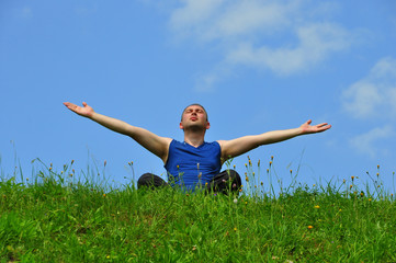 Man sitting on the grass with his hands raised up