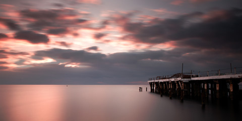 Naklejka na ściany i meble Cloudy sea sunrise with a jetty
