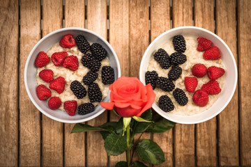 Romantic breakfast - couple of cereal bowls with berries and rose against wooden background