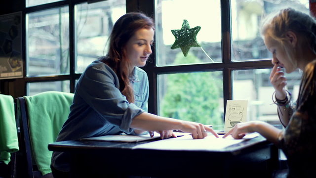 Two women sitting in the cafe and choosing meal from the menu, steadycam shot
