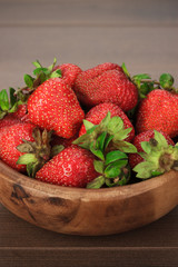 wooden bowl full of fresh strawberries on the brown table