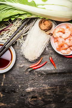Ingredients for asian cooking: rice noodles, Bok choy (chinese cabbage) , soy sauce, shrimps, chili, and chopsticks on vintage rustic background, top view, place for text. Asian food concept.