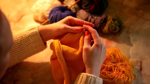 Woman sitting and knitting beautiful orange scarf, close up