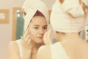Woman applying mask cream on face in bathroom