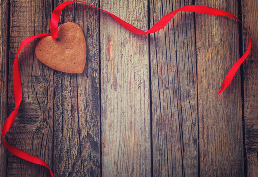 Valentine's day gingerbread heart with red ribbon on wooden background.Toned image.Vintage style.Copy space.