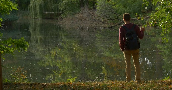 Man With Backpack Came to The Forest Lake Banck Walks Away Tourist at Overgrown Banks Rippling Water Trees' Reflection in the Water Fallen Dry Treer