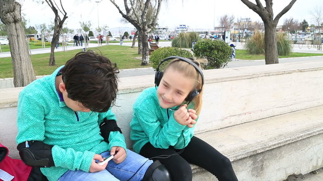 Happy cute schoolboy and schoolgirl  listening to music in outdoors
