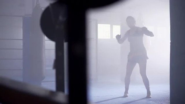 Female muay thai boxer shadowboxing in a boxing club with a ring at background. Dolly move. UHD, 4K.