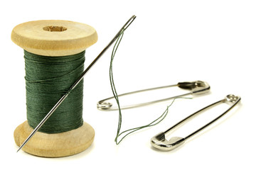 Wooden coil with threads, needle and safety pin for sewing on a white background