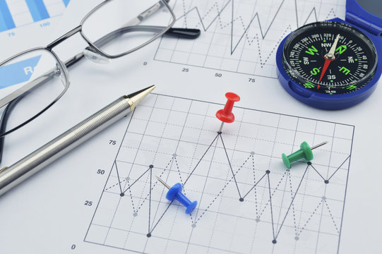 Red pin, blue compass, pen and glasses on graph paper, success c