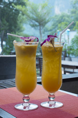Two glasses of fruit cocktail decorated with orchid flower on the table