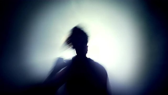 Silhouette of a female boxer training, making shadowboxing with a strong light behind her. UHD, 4K.