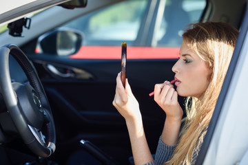 Blonde woman applying lipstick looking at mirror in her car