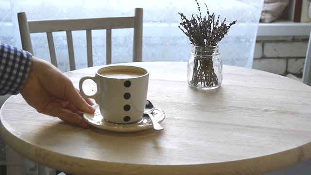 A man puts a cup of coffee on the table in slowmotion