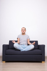 meditation concept - tired man sitting on sofa in yoga pose