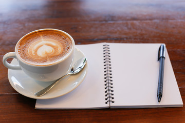 Coffee cup and notebook on table background.