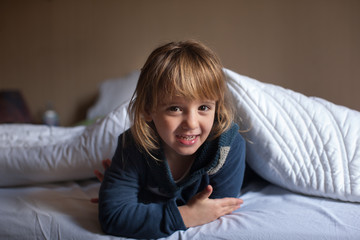Bambina gioca a letto sotto il piumone