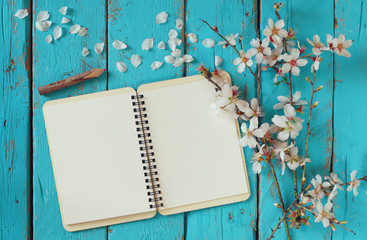 top view image of spring white cherry blossoms tree, open blank notebook  next to wooden colorfull pencils on wooden table. vintage filtered and toned image
