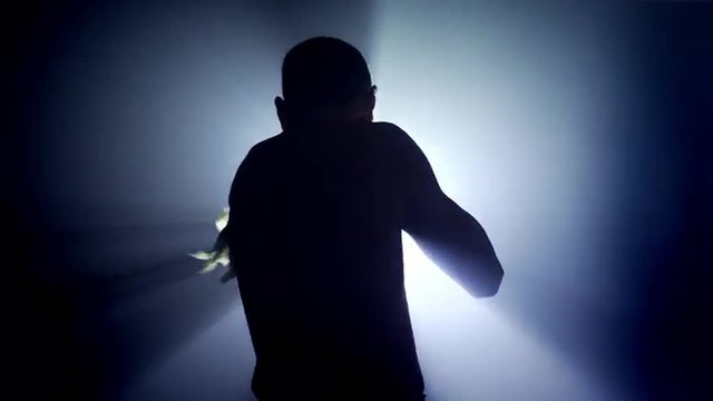 Silhouette of a male boxer training with his back towards camera, making shadowboxing with a strong light behind him. UHD, 4K.