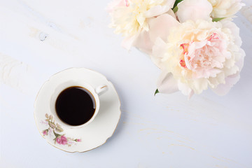 Still life with cup of coffee and flowers (peonies) on light  lilac wooden table.