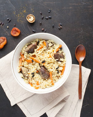 oriental dish called plov made of lamb, rice, garlic, carrots, onion and flavored with jeera, saffron and barberry on worn brown and black background