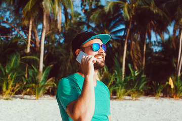 young handsome man with beard and mustache in baseball cap, with a smartphone in his hand talking on the phone, hipster style, outdoor portrait, close up