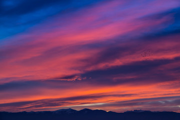 Sunset / sunrise with vivid magenta sky, clouds and mountains dark silhouettes.