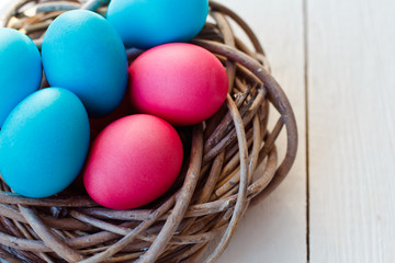 Fototapeta na wymiar blue and pink Easter eggs in nest on white wooden background